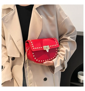 Détail du sac selle en cuir rouge avec clous dorés et bandoulière sur trench-coat beige