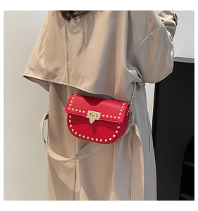 Detailed view of a red pebble leather saddle bag with gold studs and chain strap