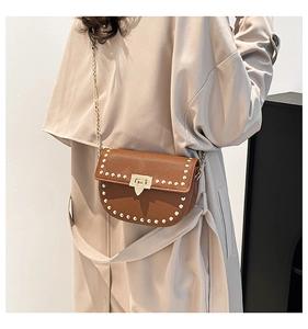 Close-up of brown pebbled leather saddle bag with gold studs and metal chain strap