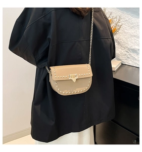 Detailed view of khaki rivet crossbody bag with gold chain strap on a model shoulder