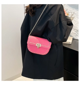 Détail du sac à rabat rose à rivets avec bandoulière chaîne sur un blazer noir