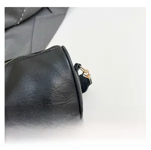 Detail of black leather cylinder bag with gold metallic zipper and logo patch