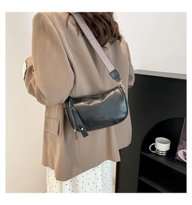 Detail of black semi-moon crossbody bag with patterned strap and fashion logo