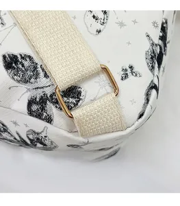 Detail of a white canvas backpack featuring a golden metal buckle and black butterfly prints