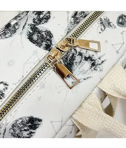 Detail of gold double-zipper system on a white leather backpack with butterfly prints