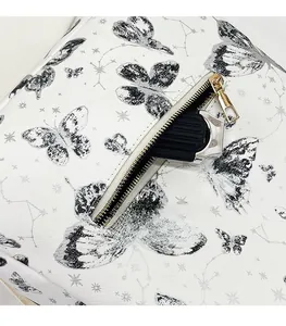 Detail of white backpack with butterfly print showing gold zipper and storage space