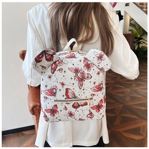Detail of white backpack with red butterfly and star patterns on a model in a cafe