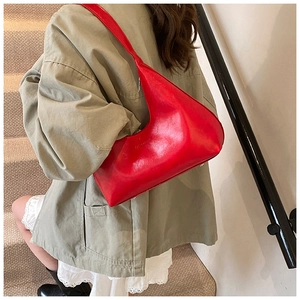 Vibrant red hobo bag with sleek glossy finish worn by a model in a casual setting