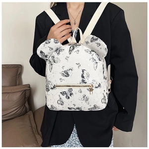 Detail view of white backpack with bow patterns and signature round ears on black blazer