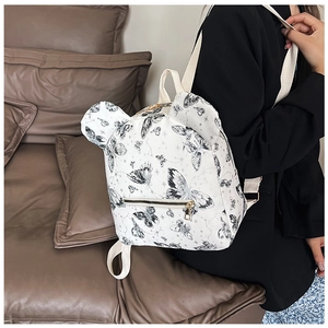Detail of white butterfly print backpack with ear accents worn over a black blazer