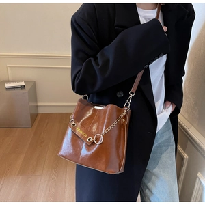 Close-up of brown bucket bag with shiny faux leather texture and gold chain detail