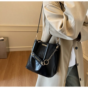 Detail of black leather bucket bag featuring gold fashion lettering on the shoulder strap