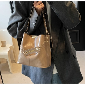 Detailed view of camel leather bucket bag with gold chain and fashion hangtag decor