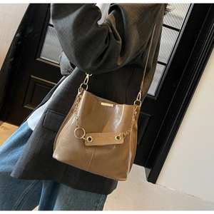 Detail of tan leather bucket bag with gold chain strap and fashion tag on model