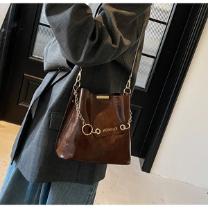 Detailed side view of brown leather bucket bag with gold chain and fashion patch