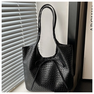 Detail of black woven leather tote bag with bow accent on a minimalist window sill