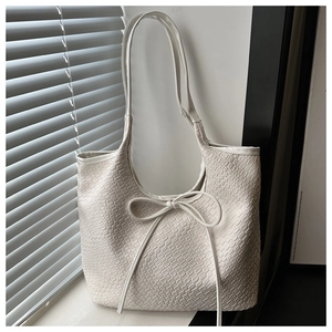 Detail view of cream-white tote bag featuring delicate woven texture and bow tie accent