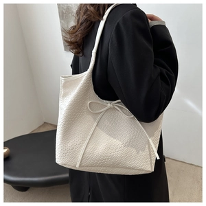 Detail of off-white woven tote bag with bow drawstring on a black blazer