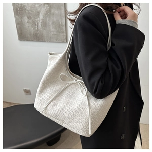 Detail of white woven leather tote bag featuring thin drawstring bow accents on black blazer
