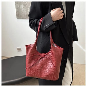 Detail of a dark red woven tote bag with leather bow decoration and Intrecciato texture
