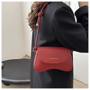 Detail of red crescent shoulder bag featuring a knotted strap and gold fashion lettering