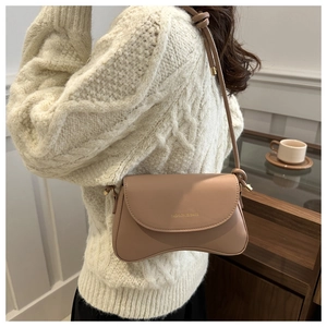 Close-up of a stylish beige shoulder bag with a unique wave-shaped base and metal buckle