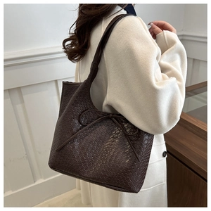 Detail of dark brown woven tote bag featuring a decorative bow on the shoulder strap