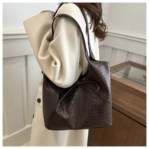 Detail of dark brown woven leather tote bag featuring a decorative ribbon bow