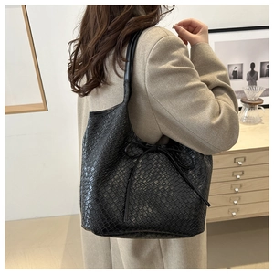 Side view of a black woven leather tote bag with elegant bow detail on female model