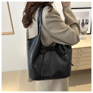 Detail of black woven leather tote bag with thin bow accent on a female model shoulder
