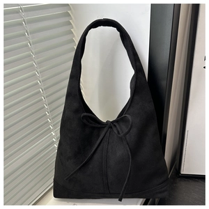 Detail of a black suede hobo tote bag with a bow tie, shown in soft window light