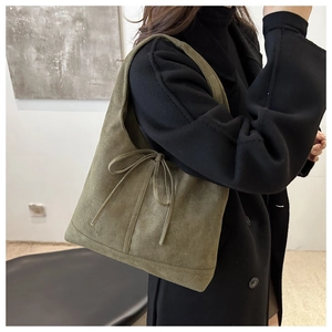 Detail of dark green suede tote bag with bow decoration worn on the shoulder by a model