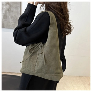 Detail of dark green suede tote bag with drawstring bow on minimalist gray background