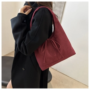 Burgundy suede tote bag with bow detail worn by a model in a black wool coat