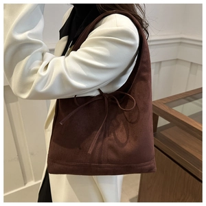 Detail of dark brown suede tote bag featuring a decorative side bow on a white blazer