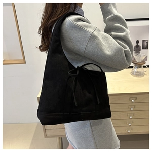 Side view of black hobo bag with bow drawstring detail worn by a model in interior