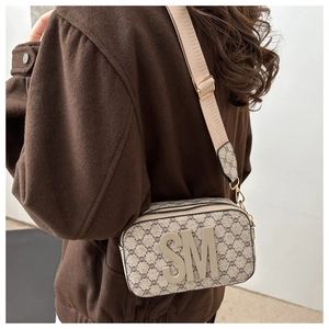 Macro shot of camera bag showing vintage monogram pattern and wide fabric strap