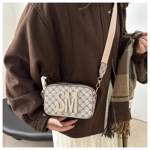 Detail of crossbody camera bag with monogram pattern and large metallic SM letter ornament