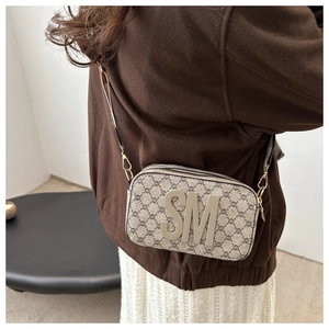Detail of a vintage-style monogram camera bag with gold SM hardware and zip closure