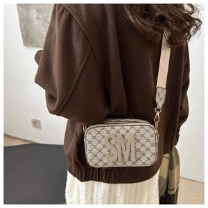 Detailed side view of camera bag with wide strap and embossed SM logo on textured fabric