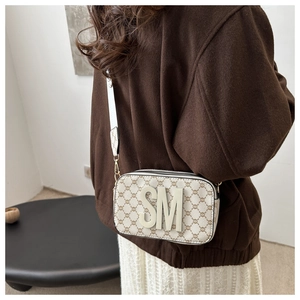 Detail of camera bag showing wide strap and 3D SM letter on beige monogram canvas