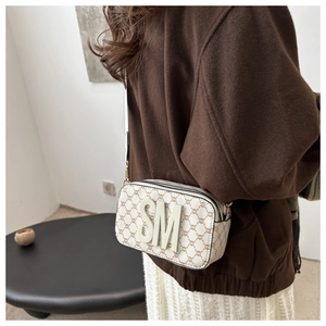 Detail of cream camera bag featuring vintage logo print and white 3D SM letter emblem