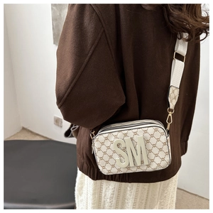 Detail of crossbody camera bag with wide strap, metal logo, and mini pouch attachment