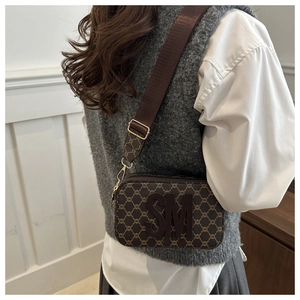 Brown monogram camera bag with SM lettering and adjustable wide strap on female model