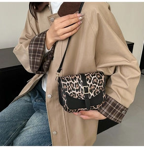 Detail of leopard print crossbody bag with black leather trim and golden metal buckle