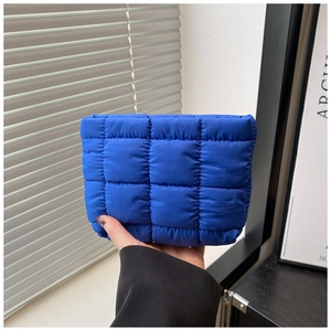 Close-up of bright blue quilted puffer pouch held by hand showing nylon texture and size