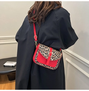 Detail of red crossbody saddle bag with leopard print flap and golden buckle on model