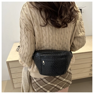 Detail of black woven crescent belt bag with gold zipper shown on a model