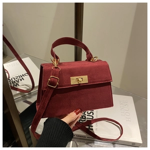 Close-up of a burgundy suede handbag featuring a gold lock and adjustable strap