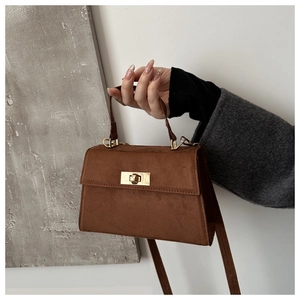 Detail view of brown faux suede crossbody bag featuring a golden metallic twist lock closure
